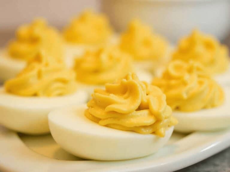 Deviled eggs with creamy mustard filling on white serving platter for healthy snack.