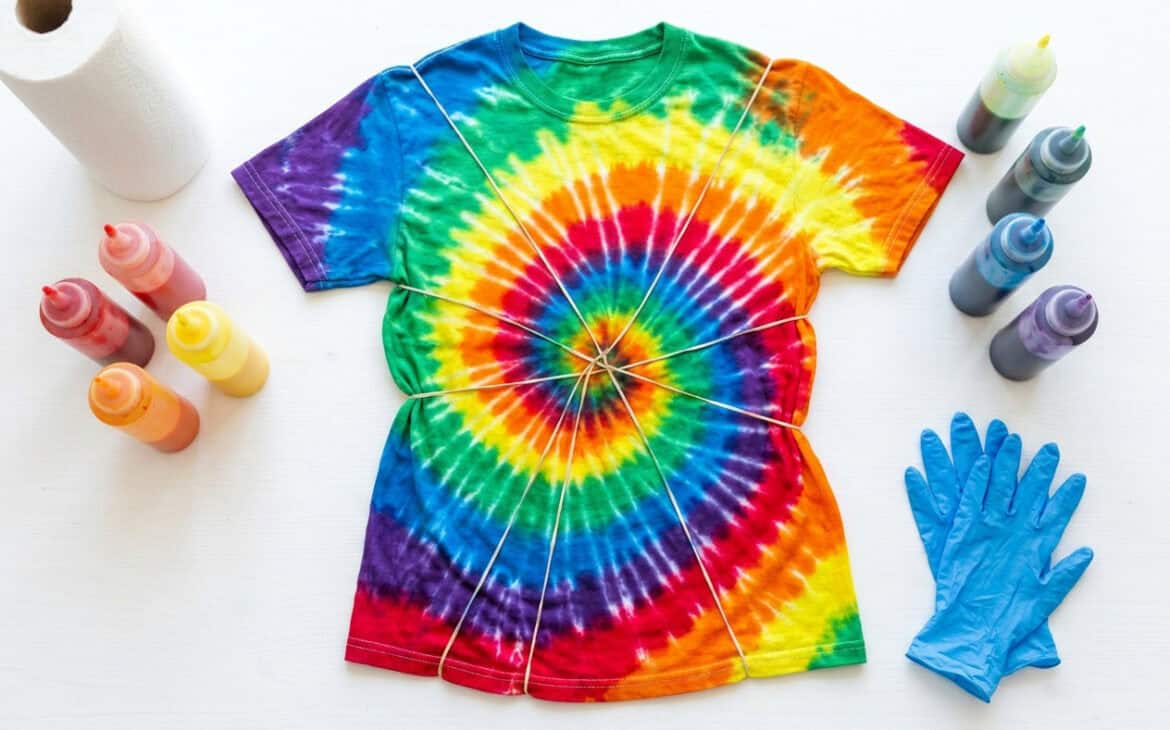 A rainbow spiral tie-dyed shirt surrounded by dye bottles and blue nitrile gloves