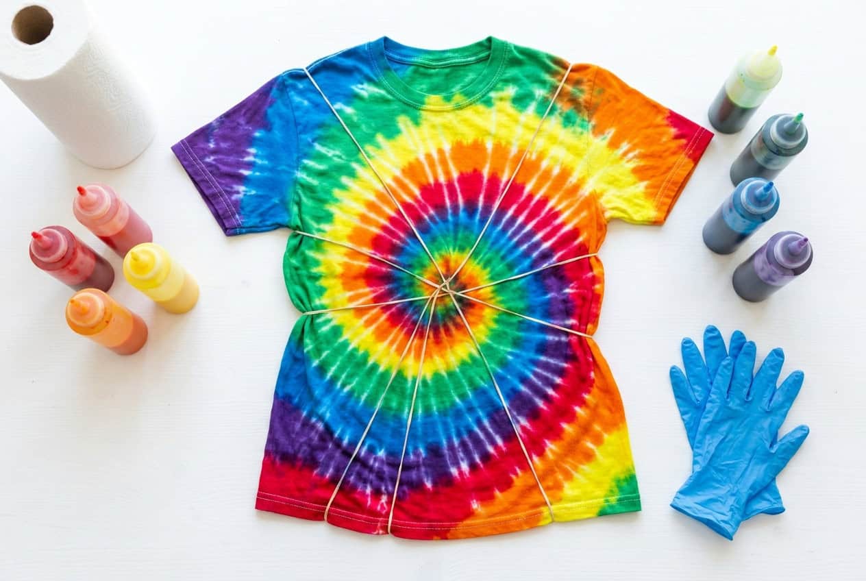 A rainbow spiral tie-dyed shirt surrounded by dye bottles and blue nitrile gloves